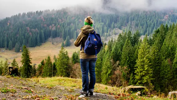 Eine Frau steht auf einem Wanderweg und schaut auf die Landschaft.