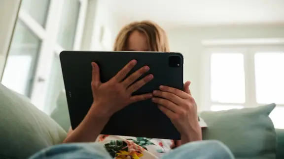 Ein Mädchen sitzt auf der Couch und guckt auf ein Tablet (Themenbild).