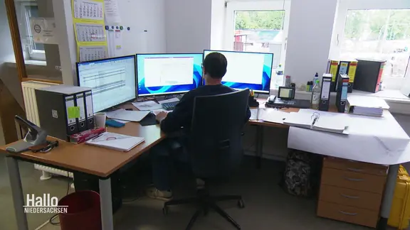 Ein Mann sitzt vor drei Bildschirmen in einem Büro.