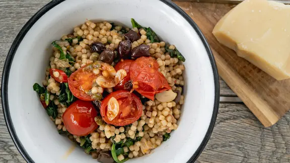 Fregola sarda mit Spinat und Tomaten auf einem Teller serviert
