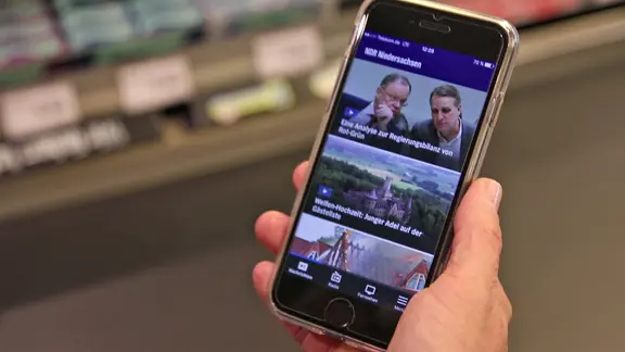 Ein Smartphone mit der geöffneten NDR App wird in der Hand gehalten.