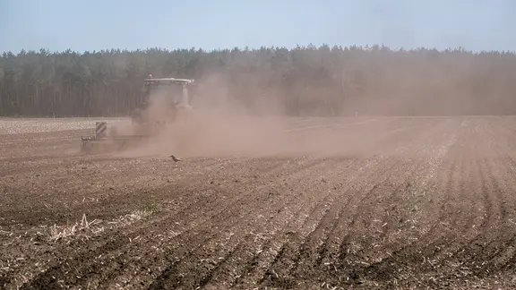 Ein Bauer fährt mit einer Landmaschine über ein staubiges Feld.