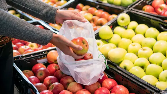 Eine Supermarktkundin legt Äpfel in ein Mehrwegnetz