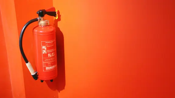 Feuerlöscher, an einer orangenen Wand befestigt.