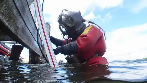 Ein Taucher steigt in einem alten Anzug ins Wasser.