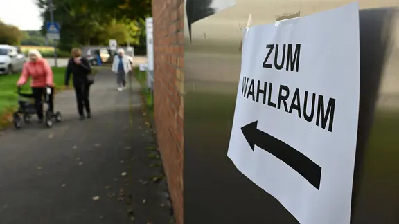 Ein Zettel mit der Aufschrift "Zum Wahlraum" hängt an einem Wahllokal.