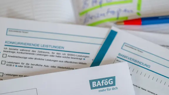 Unterlagen für einen BAföG-Antrag und ein Stift liegen auf einem Tisch. 