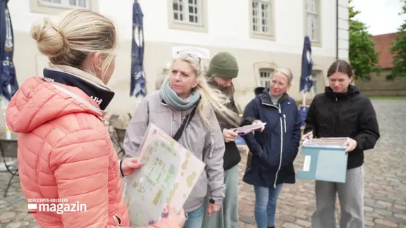 Vier Menschen im Gespräch. Eine Frau hält einen Lageplan der Museumsinsel Schleswig in der Hand.