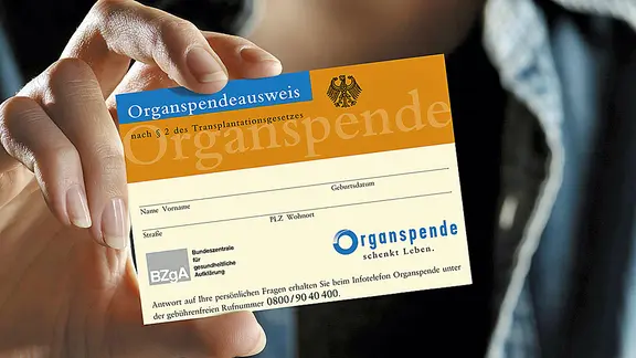 Eine Frau hält einen Organspendeausweis in die Höhe.