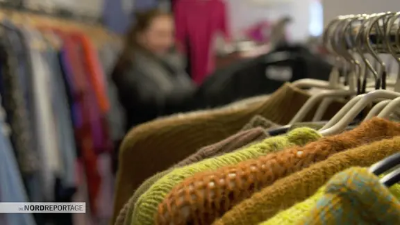 Wollpullover hängen an Kleiderbügeln in einem Second-Hand-Laden.