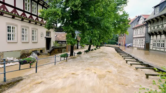 Überschwemmte Straße mit einem über die Ufer getretenen kleinen Bach, der nun ein reißender Fluß ist, bei einem Hochwasser in Goslar im Harz (26.07.2017).