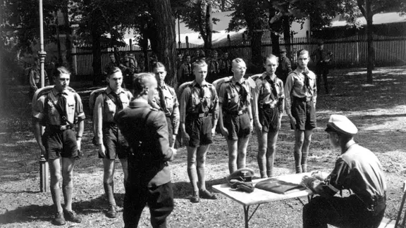 Mitglieder der Hitler-Jugend stehen in einer Reihe vor ihrem Vorgesetzten.