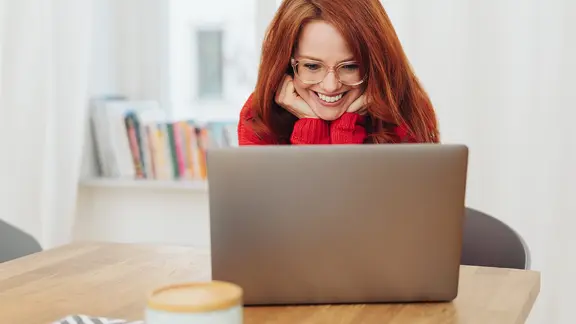 Eine rothaarige Frau blickt lächelnd in einen Laptop