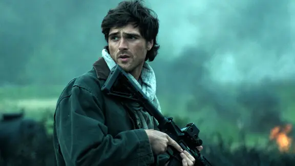 Szene aus dem Film "Das Ende der Sterne": Ein junger Mann steht mit einer Waffe in der Hand auf einem Feld und blickt besorgt zur Seite