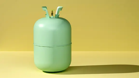 Eine grüne Gasflasche vor gelbem Hintergrund.