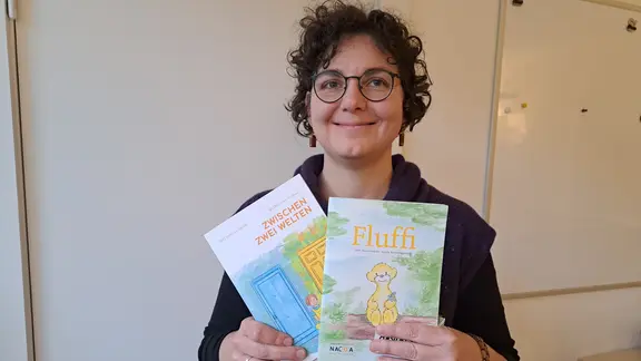 Eine hält lächelnd drei Kinderbücher in der Hand.