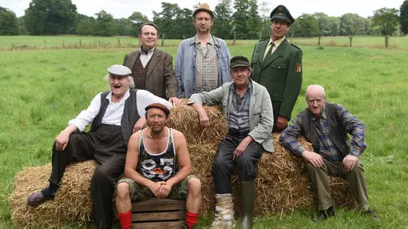Onkel Krischan, Günther Griem, Adsche, Polizist Peter, Kuno, Brakelmann und Shorty sitzen und stehen auf Strohballen.