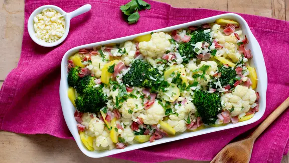 Brokkoli-Blumenkohl-Auflauf und ein Schälchen mit geriebenen Käse liegen auf einem Tisch.
