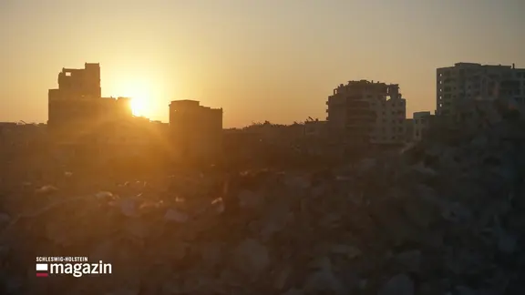 Zerstörte Häuser und Trümmer in Syrien vor einem Sonnenuntergang.