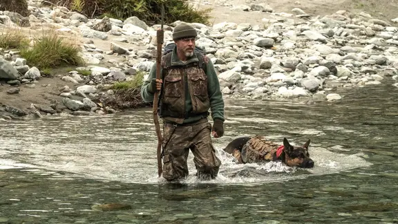 Szene aus dem Film "Eiserne Wildnis - Heart Of The Beast": Ein Mann und ein Schäferhund überqueren einen Fluss