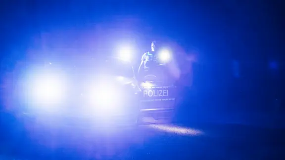 Ein Polizist steht mit einer Taschenlampe neben seinem Dienstfahrzeug.