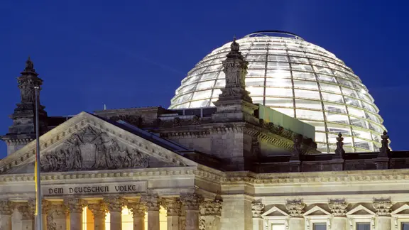 Reichstag mit hell erleuchteter Kuppel im nächtlichen Berlin.