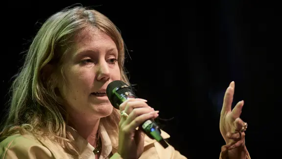 Die Autorin Jovana Reisinger sitzt auf einer Bühne uns spricht in ein Mikrofon