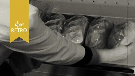 Ein Verkäufer legt in Plastikfolie verpackte Brote in eine Auslage. (1965)