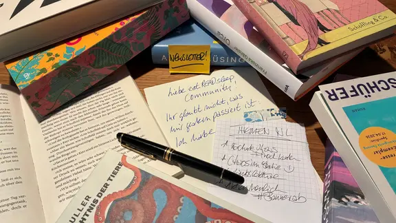 Notizen, ein Füller und Bücher liegen auf einem Tisch