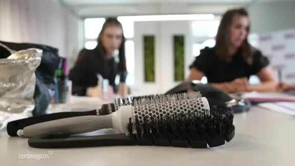Frisierbürtsen im Vordergrund, im Hintergrund unscharf zwei junge Frauen.