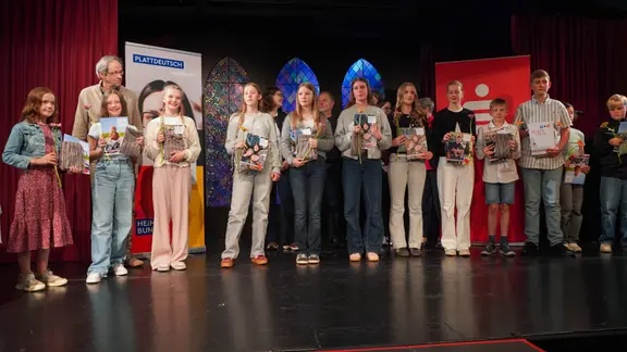 Viele Schülerinnen und Schüler stehen auf einer Bühne.