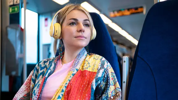 Eine Frau mit gelben Kopfhörern sitzt in einem Regionalzug.