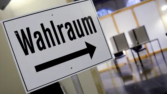 Ein Schild mit der Aufschrift "Wahlraum" und einem Richtungspfeil.