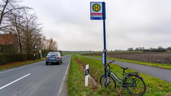 Bushaltestelle auf dem Land, abgestelltes Fahrrad und vorbeifahrendes Auto
