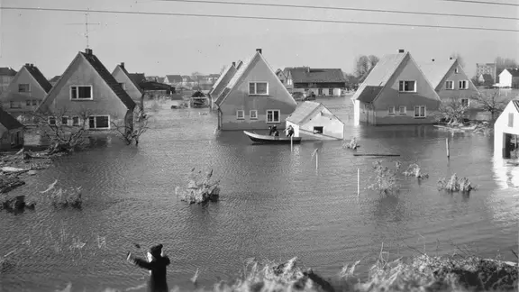 Ein Boot fährt nach der Sturmflut 1962 an Siedlungshäusern am Sandwisch in Moorfleet vorbei.