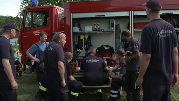 Die Truppe der freiwilligen Feuerwehr Bollensen sitzt gemeinsam an einem Einsatzwagen.