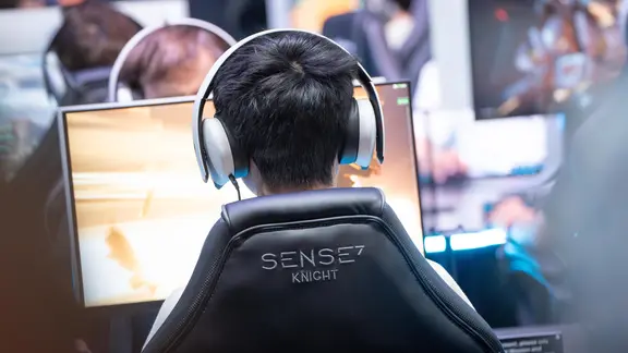 Jugendliche sitzen mit Headsets vor Computerbildschirmen und spielen Videospiele