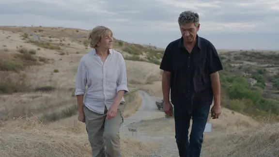 Szene aus dem Film "Das geträumte Abenteuer": Eine Frau und ein Mann gehen nebeneinander einen schmalen Pfad entlang, der durch eine hügelige Landschaft führt.