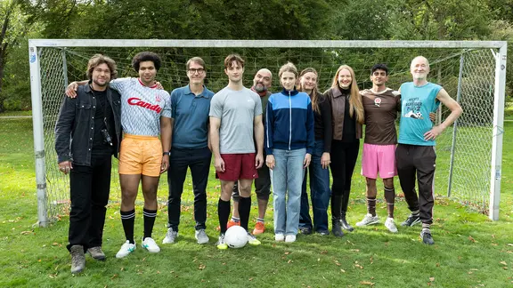 Eine Gruppe Menschen steht vor einem Fußballtor und schaut in die Kamera