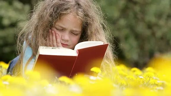 Ein Mädchen liest auf einer Wiese ein Buch.