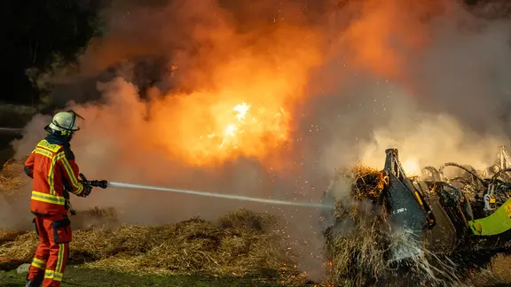 Einsatzkräfte der Feuerwehr löschen einen Stroballen-Brand.