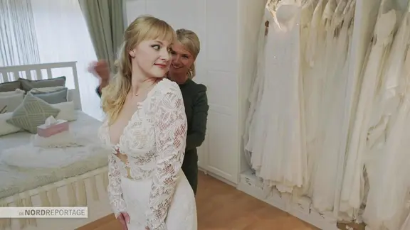Eine Frau probiert in einem Schlafzimmer ein Hochzeitskleid an.