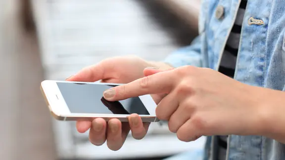 Mädchenhand tippt auf einem Smartphone.