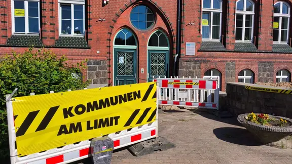 Gelbes Plakat an Baustellenabsperrung vor Rathaus
