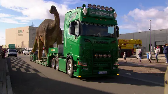 Eine Dino-Figur steht auf einem Lkw.