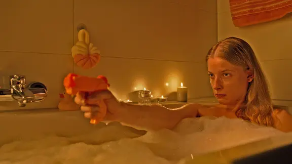 Eine Frau sitzt in der Badewanne mit einer Wasserpistole in der Hand