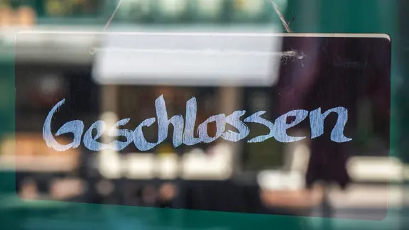 Ein Schild mit dem Wort "geschlossen" hängt hinter einer Glastür.