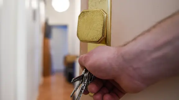 Ein Mann schließt eine Wohnungstür auf und öffnet sie, dahinter liegt der Flur.