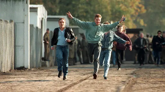 Jubelnd laufen drei junge Ost-Berliner am 10. November 1989 durch einen Berliner Grenzübergang.