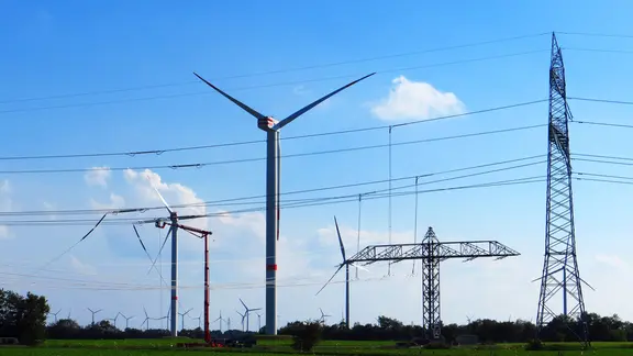 Windkraftanlagen zwischen Stromleitungen auf einer großen Wiese